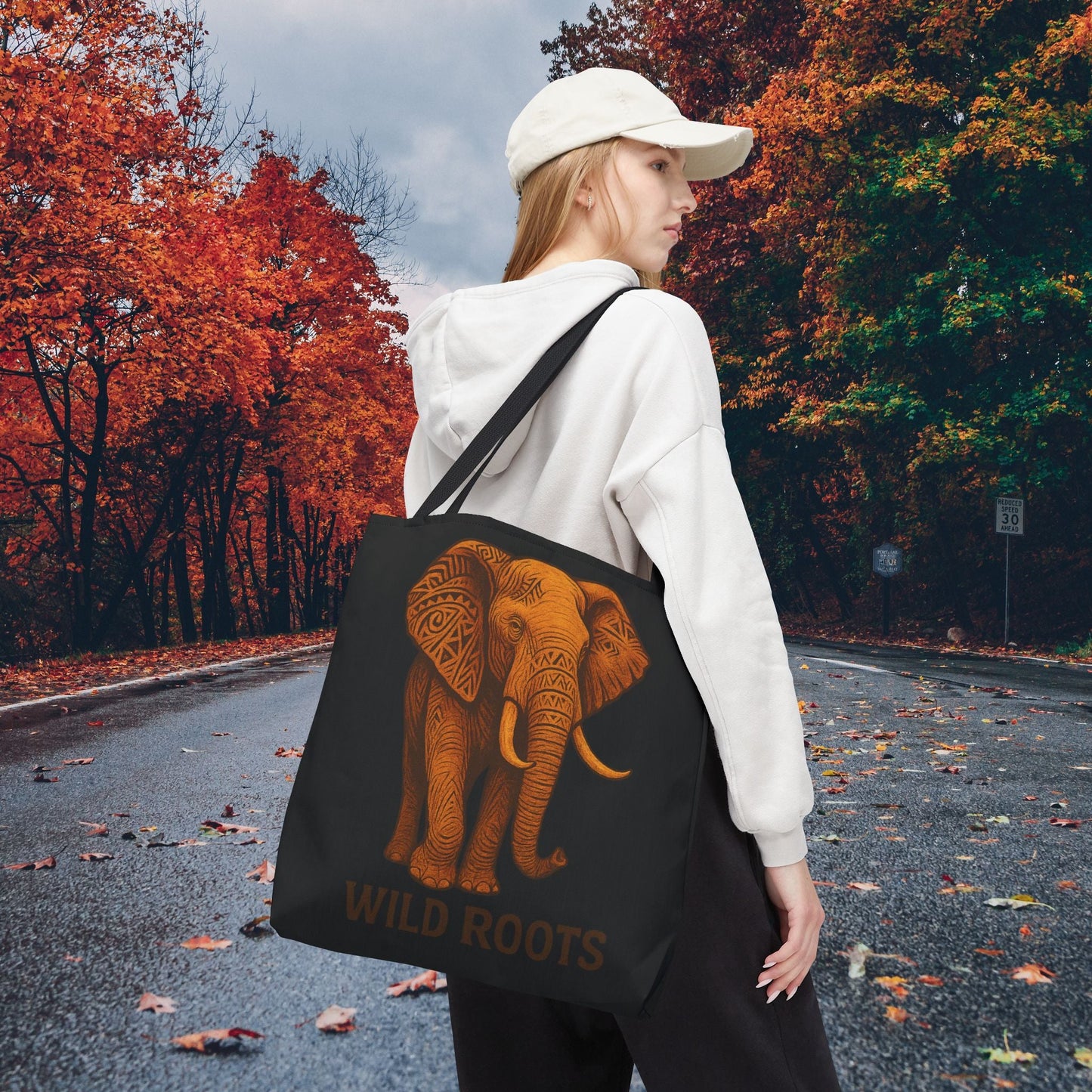 Black Mashafrica tote bag featuring orange tribal elephant Wild Roots print carried by woman on autumn road