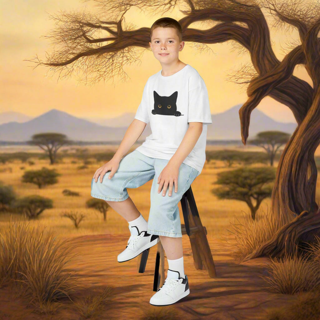 Mashafrica kids white t shirt with black peeky cat graphic modeled by boy sitting in savanna backdrop