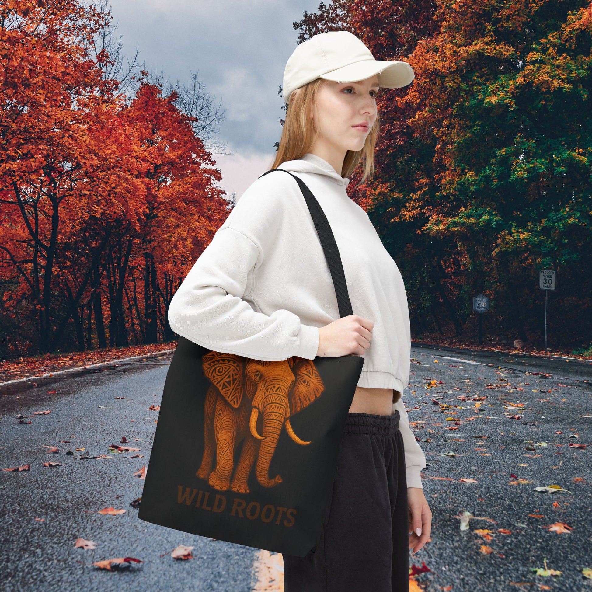Mashafrica black tote bag with orange elephant Wild Roots print carried by woman in white cap on autumn road